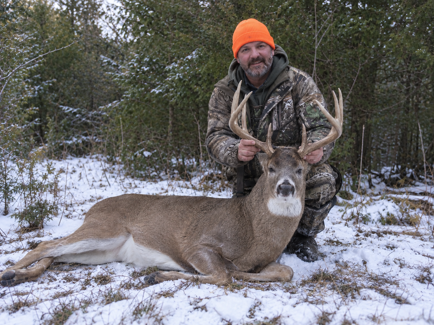 Hunter with a harvested ten-point whitetail buck in snow